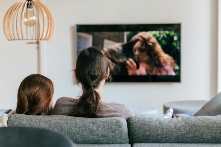 Kvinna och flicka sitter i soffan och tittar på tv.